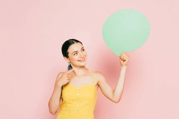 Brünette junge Frau mit grüner leerer Sprechblase auf rosa — Stockfoto