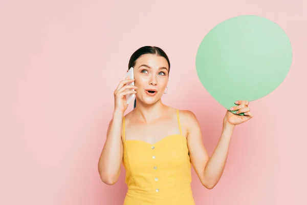 Sorpresa bruna giovane donna con verde bolla discorso in bianco parlando su smartphone su rosa — Foto stock