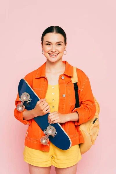 Brünette junge Frau in buntem Outfit mit Skateboard isoliert auf rosa — Stockfoto