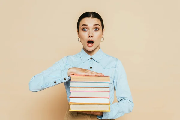 Shocked student in denim shirt with books on beige — Stock Photo