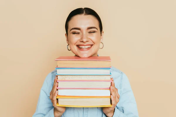 Estudiante en camisa de mezclilla con libros sonriendo aislado en beige - foto de stock