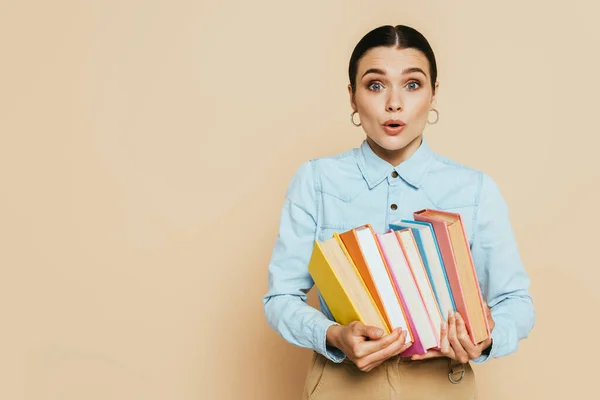 Shocked student in denim shirt with books on beige — Stock Photo