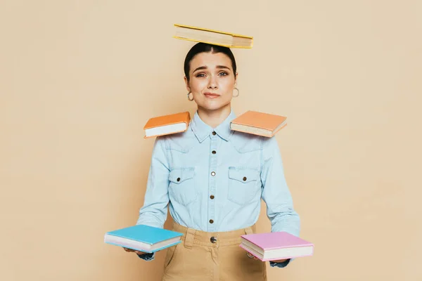 Estudante cético em camisa jeans com livros sobre corpo isolado em bege — Fotografia de Stock