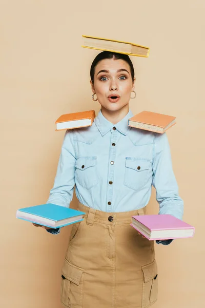 Shocked student in denim shirt with books on body on beige — Stock Photo