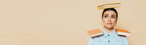 Skeptical student in denim shirt with books on head and shoulders isolated on beige, panoramic shot — Stock Photo