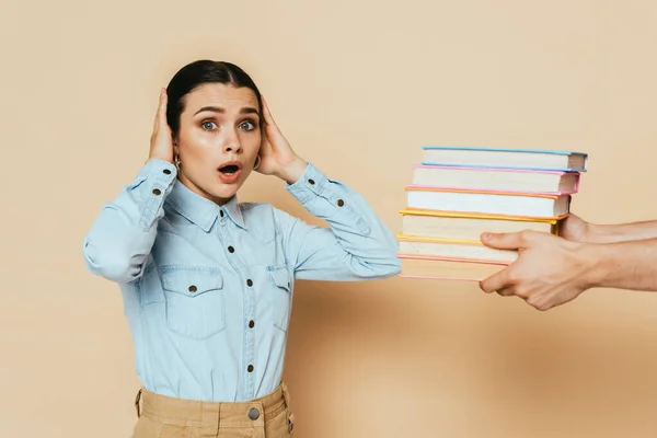 Shocked student in denim shirt near books on beige — Stock Photo
