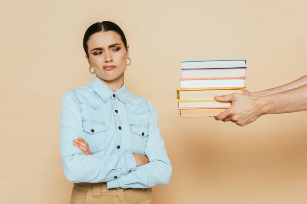 Skeptischer Student im Jeanshemd schaut sich Bücher auf beige an — Stockfoto