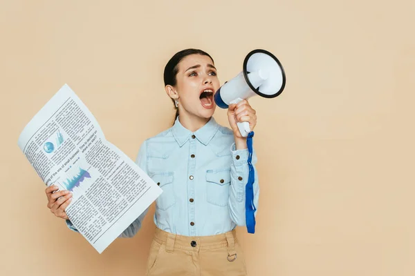 Brunette woman in denim shirt with newspaper screaming in loudspeaker isolated on beige — Stock Photo