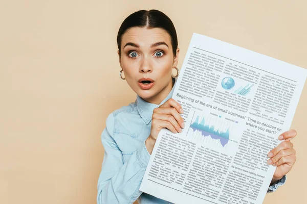 Femme brune choquée en chemise denim avec journal d'affaires isolé sur beige — Photo de stock