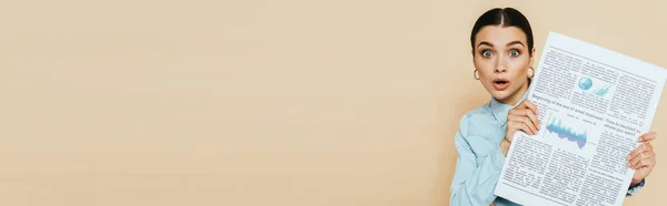 Femme brune choquée en chemise denim avec journal d'affaires isolé sur beige, vue panoramique — Photo de stock