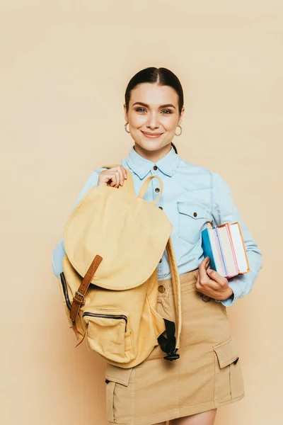 Étudiante brune en chemise denim avec livres et sac à dos isolé sur beige — Photo de stock