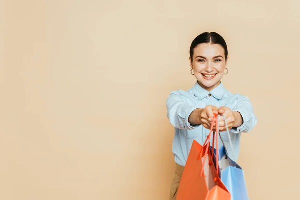 Brünette Frau im Jeanshemd gibt Einkaufstüten auf beige — Stockfoto
