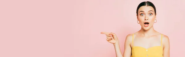 Шокована брюнетка молода жінка вказує в сторону на рожевий, панорамний постріл — стокове фото