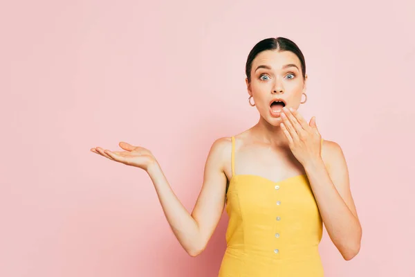 Choqué brunette jeune femme pointant avec la main de côté et couvrant la bouche sur rose — Photo de stock