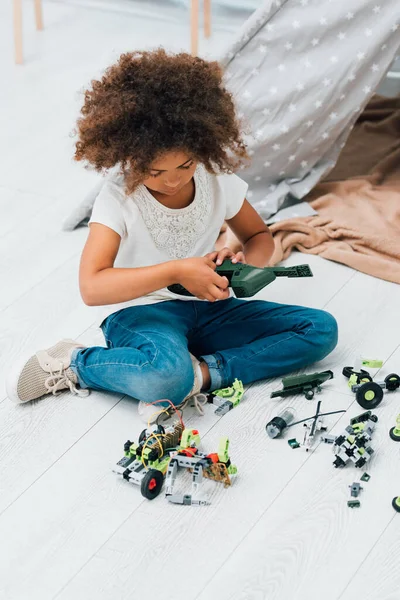 Кучерява афроамериканська дитина грає з пластиковими іграшками і сидить на підлозі — стокове фото