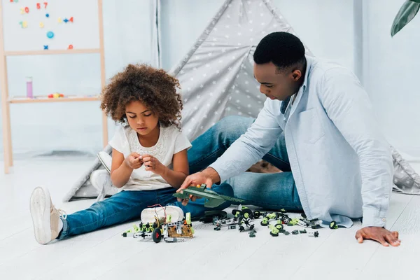 Afro-americano pai e criança sentado no chão e brincando com brinquedos de plástico — Fotografia de Stock