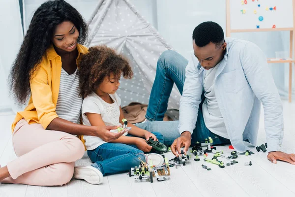 Афроамериканські батьки сидять на підлозі з дочкою біля пластикових іграшок — стокове фото