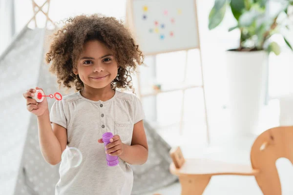 Curly african american kid looking at camera near shiny soap bubble — Stock Photo