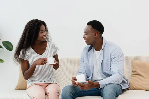 African american couple holding cups of coffee and sitting on sofa — Stock Photo