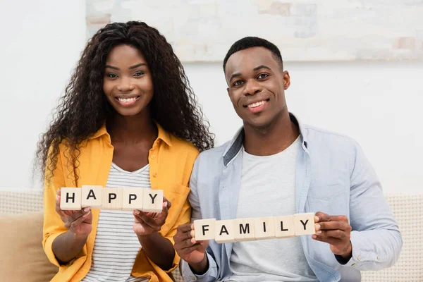 African american man and brunette woman holding wooden cubes with happy family lettering — Stock Photo