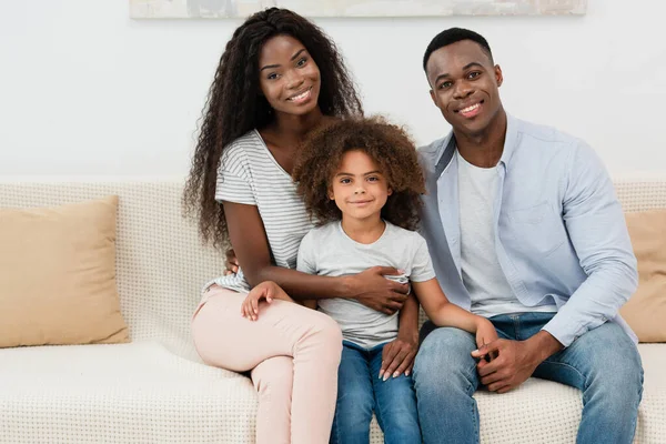 Afrikanisch-amerikanische Familie blickt in die Kamera und sitzt auf dem Sofa im Wohnzimmer — Stockfoto