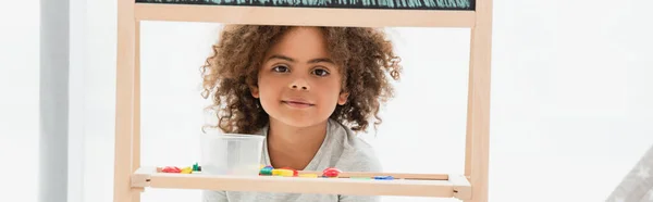 Panoramic crop of curly african american kid near wooden frame — Stock Photo