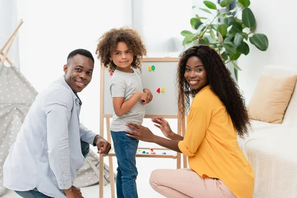 African american family looking at camera near magnetic easel — Stock Photo