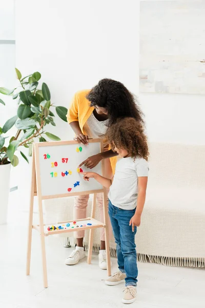 Afro-americana madre e figlia puntando con le dita ai magneti sulla lavagna bianca — Foto stock