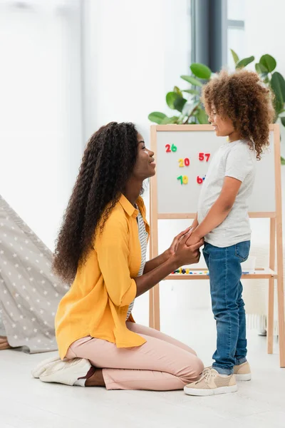 Vista lateral de la madre y la hija afroamericanas cogidas de la mano en casa - foto de stock