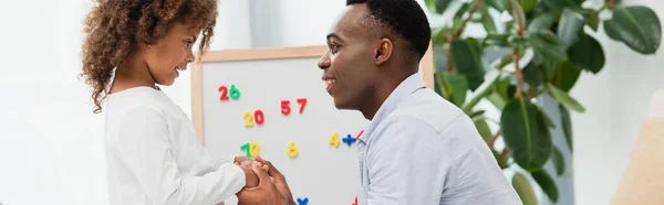 Panoramic crop of african american father and daughter holding hands at home — Stock Photo