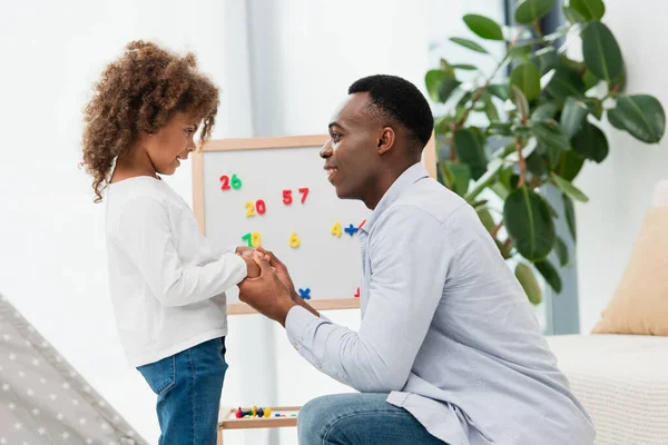 Seitenansicht eines afrikanisch-amerikanischen Vaters und seiner Tochter beim Händchenhalten zu Hause — Stockfoto