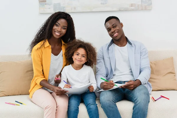 Afrikanisch-amerikanische Familie zeichnet mit Farbstiften, während sie auf dem Sofa im Wohnzimmer sitzt — Stockfoto