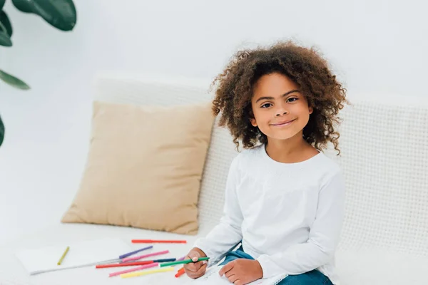 Curly african american child holding color pencil and looking at camera — Stock Photo
