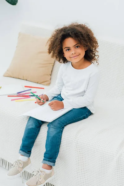 Curly african american kid holding color pencil and looking at camera — Stock Photo