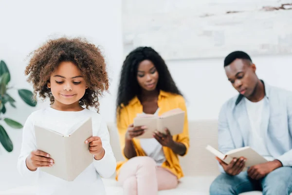 Selective focus of african american kid reading book near parents — Stock Photo