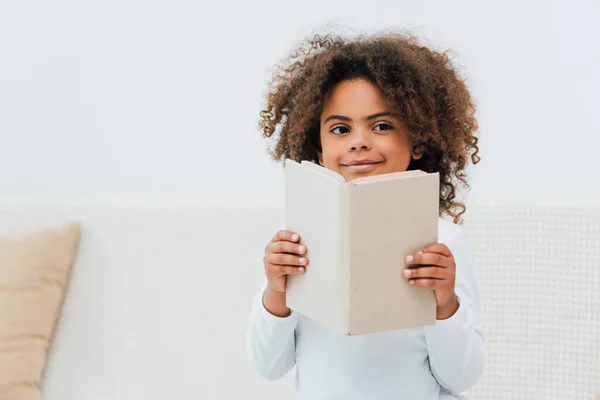 Curly african american kid holding book and looking at camera — Stock Photo