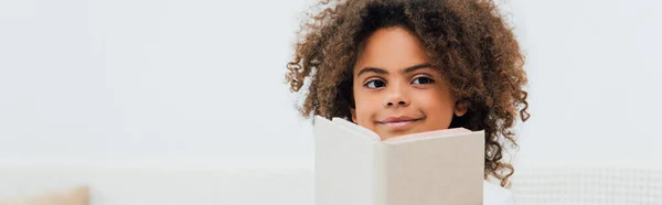 Website header of curly african american kid holding book and looking at camera — Stock Photo