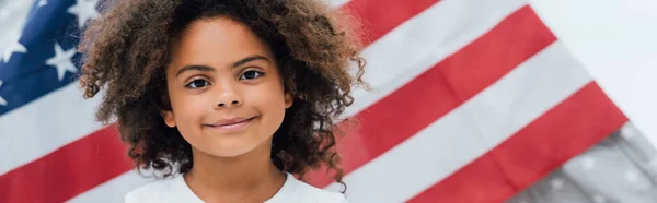 Panoramic crop of curly african american kid looking at camera near flag of america — Stock Photo
