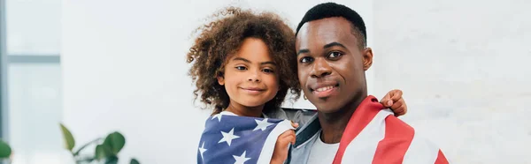 Concetto panoramico di afro-americano padre e figlia coperto di bandiera d'America guardando la fotocamera — Foto stock