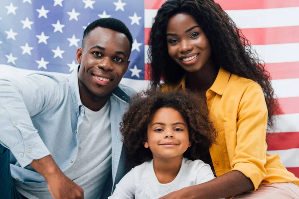 Famiglia afro-americana guardando la fotocamera vicino alla bandiera dell'America — Foto stock