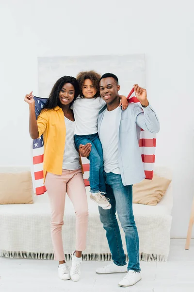 Afro-americano pai segurando em armas criança e bandeira da américa perto da esposa — Fotografia de Stock