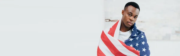 Horizontal image of african american man covered with flag of american looking at camera — Stock Photo