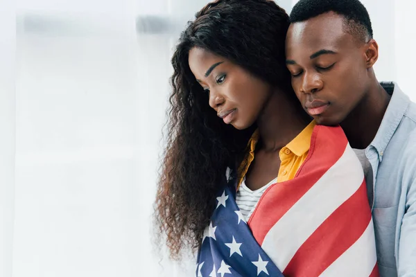 Homem americano africano com olhos fechados perto de mulher morena coberta com bandeira da américa — Fotografia de Stock