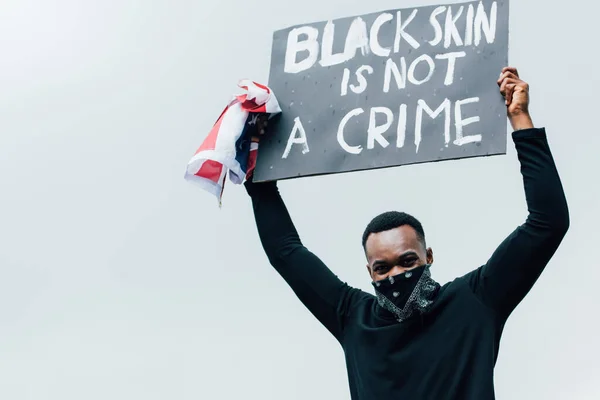 African american man holding flag of america and placard with black skin is not a crime lettering outside — Stock Photo