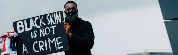 Horizontal crop of african american man holding placard with black skin is not a crime lettering and flag of america — Stock Photo