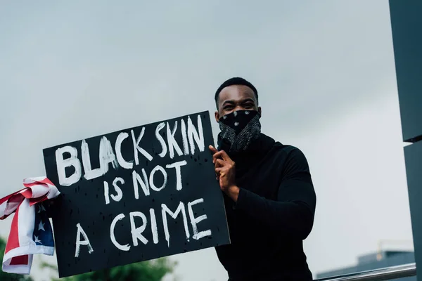 African american man holding placard with black skin is not a crime lettering and flag of america — Photo de stock