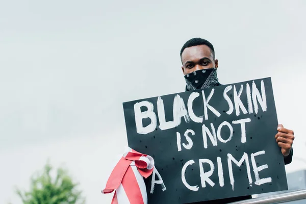 Homme afro-américain tenant une pancarte avec la peau noire n'est pas un lettrage de crime tout en regardant la caméra — Photo de stock