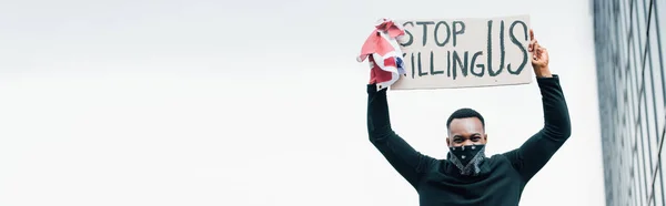 Horizontal crop of african american man holding flag of america and placard with stop killing us lettering outside — Stock Photo