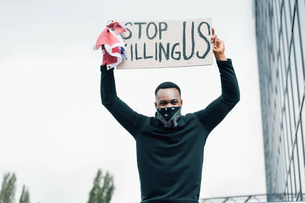 Homme afro-américain tenant drapeau d'Amérique et pancarte avec cesser de nous tuer lettrage à l'extérieur — Photo de stock