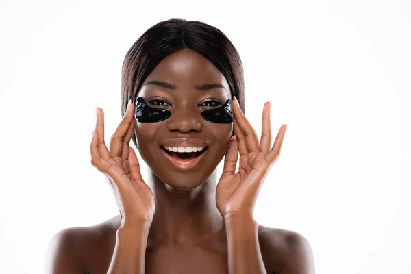 Афро-американська гола жінка торкається гідрогелевих плям очей на обличчі ізольована на білому — стокове фото